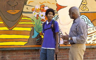 Adult male volunteer and teen against colorful mural