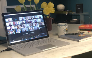 Photo of laptop showing Zoom meeting with notebook and coffee cup