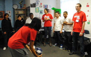 The Grassroot Project volunteers and students playing a game with a ball in a classroom