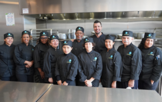 Class of culinary training students with their instructors standing in the kitchen at La Cocina VA